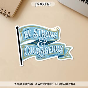 May include: A blue and white sticker with the words "BE STRONG & COURAGEOUS" in a banner design. The sticker also includes the text "Joshua 1:9". The sticker is on a light brown surface.
