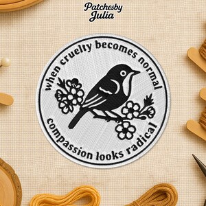 Peut inclure: Écusson brodé circulaire avec un oiseau noir sur une branche fleurie. Le texte dit : « Quand la cruauté devient normale, la compassion semble radicale ». Le patch a un fond blanc et une bordure noire.
