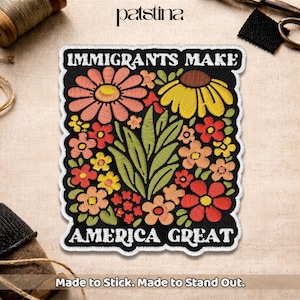 May include: Embroidered patch with the text "IMMIGRANTS MAKE AMERICA GREAT" in white on a black background. The patch features a colorful floral design with red, orange, yellow, and pink flowers and green leaves. The patch is bordered with white stitching.