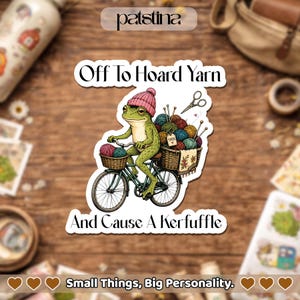 May include: A die-cut sticker featuring a green frog wearing a pink knit hat, riding a bicycle with baskets filled with colorful yarn balls and knitting needles. The text reads Off To Hoard Yarn And Cause A Kerfuffle in a dark, stylized font.