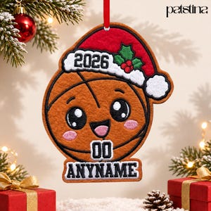 May include: A felt basketball ornament featuring a smiling face with pink cheeks, wearing a red and white Santa hat with green holly and red berries. The hat displays the year 2026, while the bottom includes the text 00 ANYNAME.