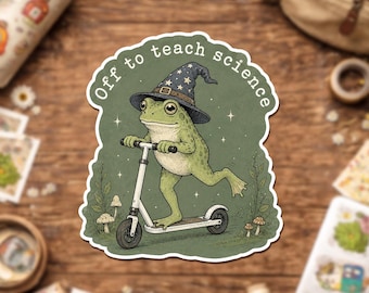 Op de afbeelding: Een gestanste sticker met een groene kikker die een donkerblauwe tovenaarshoed met gele sterren draagt en op een witte step rijdt. De tekst "Off to teach science" staat in een boog boven de kikker op een groene achtergrond met kleine paddenstoelen.