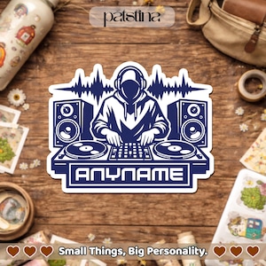 Peut inclure: Autocollant bleu marine représentant un DJ avec un casque, des platines et des enceintes. Le design comprend le texte "ANYNAME" et une onde sonore. L'autocollant est sur une surface en bois avec le texte "Small Things, Big Personality."