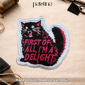 May include: Embroidered patch featuring a black cat with pink accents and the text "FIRST OF ALL, I'M A DELIGHT" in pink. The patch has a white border and is designed to be ironed on or sewn. The patch is made to stick and stand out.