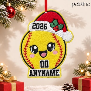 May include: A yellow felt softball ornament featuring a red Santa hat with white trim, green holly leaves, and red berries. The softball has a cartoon face, the year 2026, the number 00, and the text ANYNAME embroidered in black.