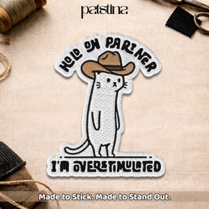 May include: Embroidered patch featuring a white cat wearing a cowboy hat, with the text "HOLD ON PARTNER" above and "I'M OVERSTIMULATED" below. The patch is designed to stick and stand out.