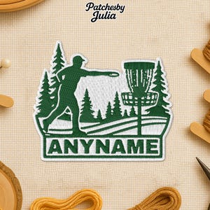 May include: Embroidered patch featuring a disc golf design with a player throwing a disc towards a basket. The patch is green and white, with the text "ANYNAME" at the bottom. The brand name "Patchesby Julia" is at the top.