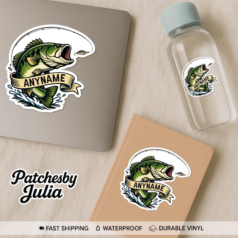 May include: A sticker featuring a green and yellow bass fish with an open mouth, a fishing rod, and the text "ANYNAME" on a banner. The sticker is displayed on a laptop, a water bottle, and a notebook.