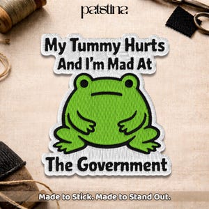 May include: Embroidered patch featuring a green frog with the text "My Tummy Hurts And I'm Mad At The Government." The patch has a white border and is designed to stick. The patch is a humorous and sarcastic statement.