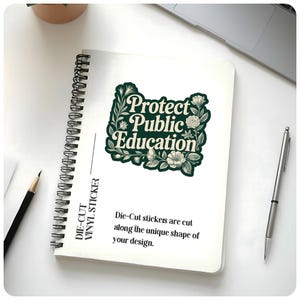 Peut inclure: Un cahier &agrave; spirales blanc avec un autocollant qui dit "Protect Public Education" dans un motif floral vert fonc&eacute;. Le cahier porte &eacute;galement le texte "Die-Cut Vinyl Sticker". Un crayon et un stylo sont &eacute;galement visibles.