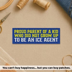 May include: A blue embroidered patch with yellow text that reads "PROUD PARENT OF A KID WHO DID NOT GROW UP TO BE AN ICE AGENT." The patch is rectangular and is surrounded by craft supplies.