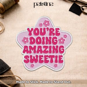 May include: A pink embroidered patch in a star shape with the words "YOU'RE DOING AMAZING SWEETIE" in bubble letters. The patch has small flower accents and a white border. The text "Made to Stick. Made to Stand Out." is at the bottom.