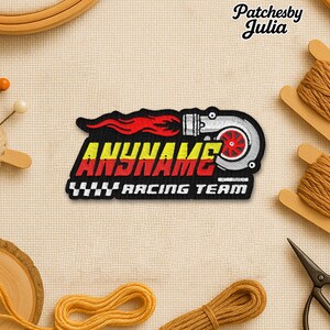 May include: Embroidered patch with a turbocharger design, the text "ANYNAME" in yellow and red, and "RACING TEAM" in white. The patch has a black background with red flames and a silver turbo. Sewing supplies, including thread and scissors, surround the patch.