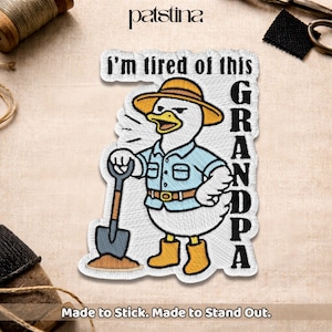 May include: Embroidered patch featuring a cartoon duck wearing a hat, shirt, and boots, holding a shovel. Text on the patch reads "I'm tired of this GRANDPA" and "Made to Stick. Made to Stand Out."