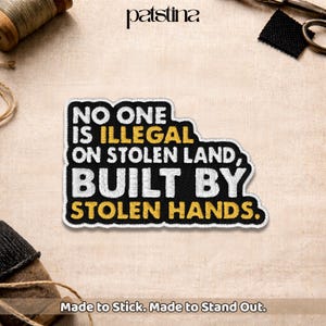 May include: Embroidered patch with the text "NO ONE IS ILLEGAL ON STOLEN LAND, BUILT BY STOLEN HANDS." The patch has a black background with white and yellow lettering and a white border. The patch is on a beige fabric.