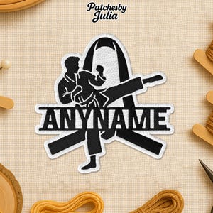 May include: Black and white embroidered patch featuring a karate figure in action, with the text "ANYNAME" below. The patch has a white border and is set against a neutral fabric background. The brand name "Patchesby Julia" is at the top.