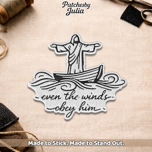 May include: Embroidered patch featuring a figure in a boat with outstretched arms, above the text "-even the winds obey him." The patch is white with black detailing. The brand name "Patchesby Julia" is at the top. The text "Made to Stick. Made to Stand Out." is at the bottom.