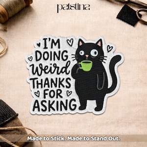 May include: Embroidered patch featuring a black cat holding a green cup, with the text "I'M DOING Weird THANKS FOR ASKING" in a whimsical font. The patch has a white border and heart accents. The text "Made to Stick. Made to Stand Out." is at the bottom.