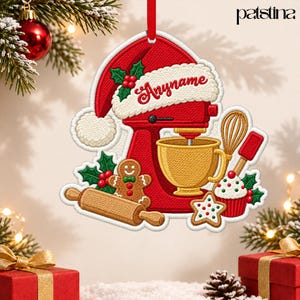 May include: A red stand mixer Christmas ornament featuring a Santa hat, a gold mixing bowl, a gingerbread man, a rolling pin, a cupcake, and holly berries. The text "Anyname" is written in red script on the white brim of the Santa hat.