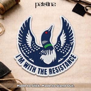 May include: Embroidered patch featuring a stylized loon with outstretched wings in navy blue, white, and green. The patch reads "I'M WITH THE RESISTANCE" in white lettering. The bottom of the patch reads "Made to Stick. Made to Stand Out."