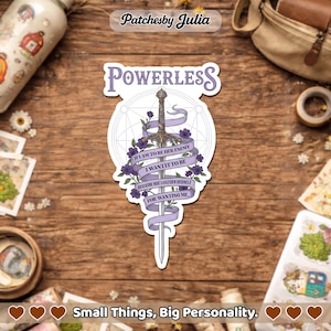 May include: A sticker with the word "POWERLESS" at the top. A sword is in the center, with a purple ribbon wrapped around it. The ribbon has text on it. Purple flowers are on the sword. The sticker is on a wooden surface.