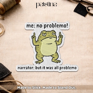 May include: Embroidered patch featuring a cartoon frog with the text "me: no problemo!" above it and "narrator: but it was all problemo" below. The frog is green and beige, giving the impression of a humorous, sarcastic design.