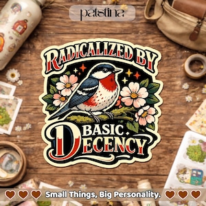 May include: A sticker featuring a bird illustration, flowers, and the text "RADICALIZED BY BASIC DECENCY." The design has a black border and is on a wooden surface. The phrase "Small Things, Big Personality" is at the bottom of the image.
