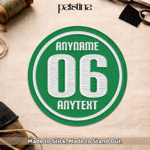 Peut inclure: Un écusson brodé vert avec du texte blanc et une bordure blanche. Le texte comprend "ANYNAME", "06" et "ANYTEXT". L'écusson est rond et porte la mention "Made to Stick. Made to Stand Out."