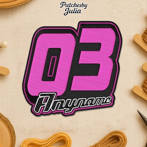 May include: Embroidered patch with the number "03" in pink, outlined in black, with the word "Anyname" below. The patch is on a beige fabric background. The text "Patchesby Julia" is at the top.