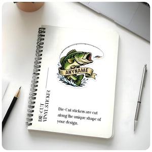 May include: A die-cut vinyl sticker featuring a green bass fish with an open mouth, a fishing lure, and the text "ANYNAME" on a banner. The sticker is on a white notebook with the text "DIE-CUT VINYL STICKER". The text "Die-Cut stickers are cut along the unique shape of your design" is also visible.