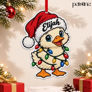 May include: A flat, embroidered Christmas ornament shaped like a duckling wearing a red Santa hat with the name Elijah written in black script. The duckling is wrapped in a string of colorful Christmas lights and has orange feet.