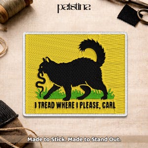 May include: Embroidered patch with a black cat carrying a snake on a yellow background. The text "I TREAD WHERE I PLEASE, CARL" is below the cat. The patch has a white border and the text "Made to Stick. Made to Stand Out."
