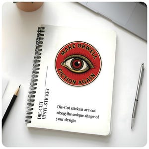 May include: A spiral-bound notebook with a sticker that reads "MAKE ORWELL FICTION AGAIN" in a red circle with an eye graphic. The notebook also has text that says "DIE-CUT VINYL STICKER". A pencil and pen are also visible.