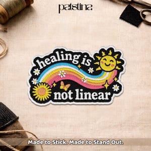 May include: Embroidered patch with the text "healing is not linear" in white on a black background. The design includes a rainbow, smiling sun, flowers, and a butterfly. The patch is made to stick.