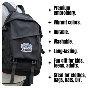 K&ouml;nnte beinhalten: Schwarzer Rucksack mit Klappenverschluss und mehreren Riemen. Der Rucksack hat einen Aufn&auml;her mit dem Text "radicalized Decency" und einem blauen Vogeldesign. Das Bild enth&auml;lt auch Text mit der Aufschrift "Premium embroidery. Vibrant colors. Durable. Washable. Long-lasting."