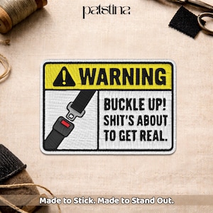 May include: Embroidered patch with a yellow and white rectangular design. The patch features a black seatbelt graphic and the text "WARNING BUCKLE UP! SHIT'S ABOUT TO GET REAL." The patch also includes the text "Made to Stick. Made to Stand Out."