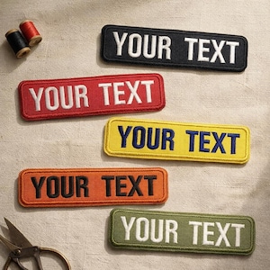 May include: Rectangular embroidered patches in black, red, yellow, orange, and olive green, each with the text "YOUR TEXT" in contrasting colors. Sewing supplies, including thread spools and scissors, are also visible.