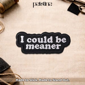 May include: Black embroidered patch with the phrase "I could be meaner" in white lettering. The patch has a wavy border and is displayed on a neutral fabric surface. The text "Made to Stick. Made to Stand Out." is at the bottom.