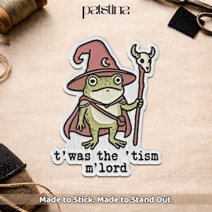 May include: Embroidered patch featuring a cartoon frog dressed as a wizard, wearing a red hat and cape, holding a staff with a skull. The text "t'was the 'tism m'lord" is below the frog. The patch is made to stick.