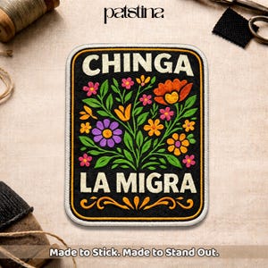 May include: Embroidered patch with a black background and a floral design. The patch features the words "CHINGA LA MIGRA" in white, with colorful flowers in orange, pink, yellow, and purple. The patch has a yellow border and the text "Made to Stick. Made to Stand Out."