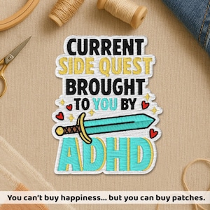 May include: Embroidered patch with the text "CURRENT SIDE QUEST BROUGHT TO YOU BY ADHD" in white, yellow, and teal. Features a teal sword with a gold hilt and red heart accents. The patch is on a beige fabric.