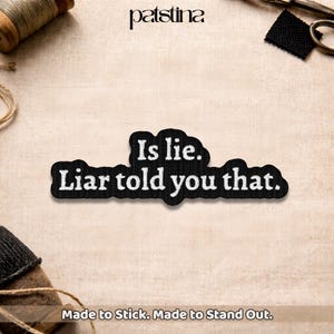 May include: A black embroidered patch with the text "Is lie. Liar told you that." in white. The patch has a unique cloud-like shape and is designed to be affixed to fabric. The brand name "patstina" is at the top.