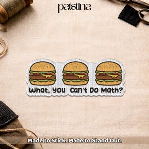 May include: Embroidered patch featuring three cartoon hamburgers with sesame seed buns, lettuce, tomato, and cheese. The text "What, You Can't Do Math?" is below the burgers. The patch is white with a stitched border.