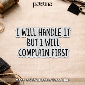 May include: A white rectangular patch with a scalloped edge featuring the black text I WILL HANDLE IT BUT I WILL COMPLAIN FIRST. The patch is positioned on a light beige fabric surface with a spool of thread and scissors visible in the corners.