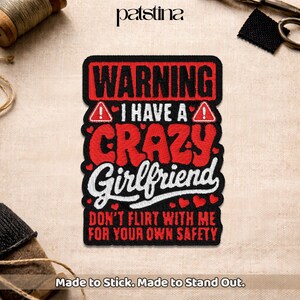 May include: A black and red embroidered patch with the text "WARNING I HAVE A CRAZY Girlfriend DON'T FLIRT WITH ME FOR YOUR OWN SAFETY". The patch has a white border and small heart details. The text "Made to Stick. Made to Stand Out." is at the bottom.