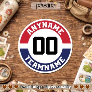 May include: A round sticker with a red and blue border, featuring the text "ANYNAME" and "TEAMNAME" in white, with the number "00" in bold black. The sticker is on a wooden surface. The text "Small Things, Big Personality" is at the bottom.