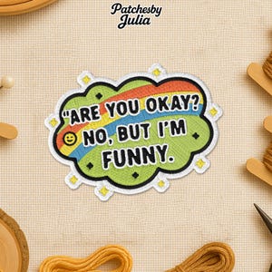 May include: Embroidered patch with the text "ARE YOU OKAY? NO, BUT I'M FUNNY." The patch has a green cloud shape with a rainbow and yellow accents. The brand name "Patchesby Julia" is at the top.