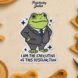 May include: Embroidered patch featuring a green frog in a gray suit and blue tie. The patch reads "I AM THE EXECUTIVE OF THIS DYSFUNCTION" in white text. The patch is surrounded by black star accents and the text "Patchesby Julia".
