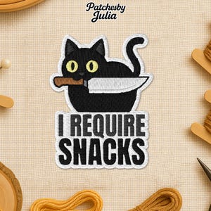 May include: Embroidered patch featuring a black cat holding a knife in its mouth. The cat has yellow eyes and is set against a white border. Below the cat, the text "I REQUIRE SNACKS" is displayed in bold, black letters.
