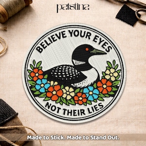 May include: Embroidered patch with a black and white loon design, surrounded by colorful flowers. The patch reads "BELIEVE YOUR EYES NOT THEIR LIES." The patch is round and has a white background. The text "Made to Stick. Made to Stand Out." is at the bottom.